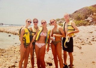 A group of young people in bathing suits and lifejackets on a rocky beach