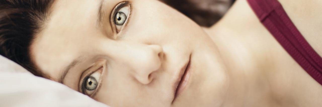 What It's Like to Relive Trauma in Your Sleep photo of woman lying in bed and staring at camera with wide eyes