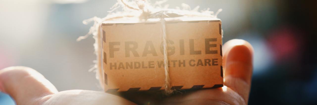 hand holding a tiny brown paper package that says "fragile open with care"