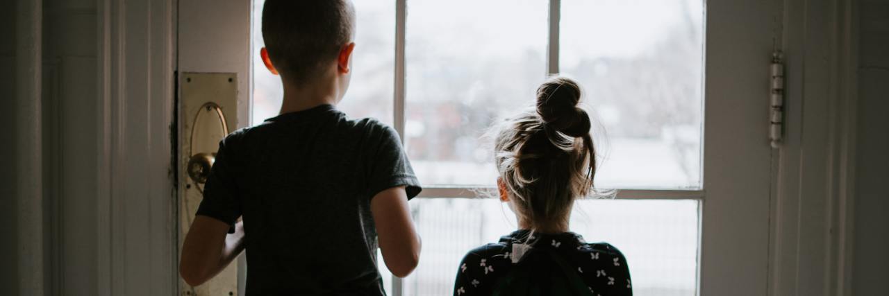 How to Talk to Children About the Coronavirus Pandemic photo of two children from behind looking outside through glass door during coronavirus quarantine