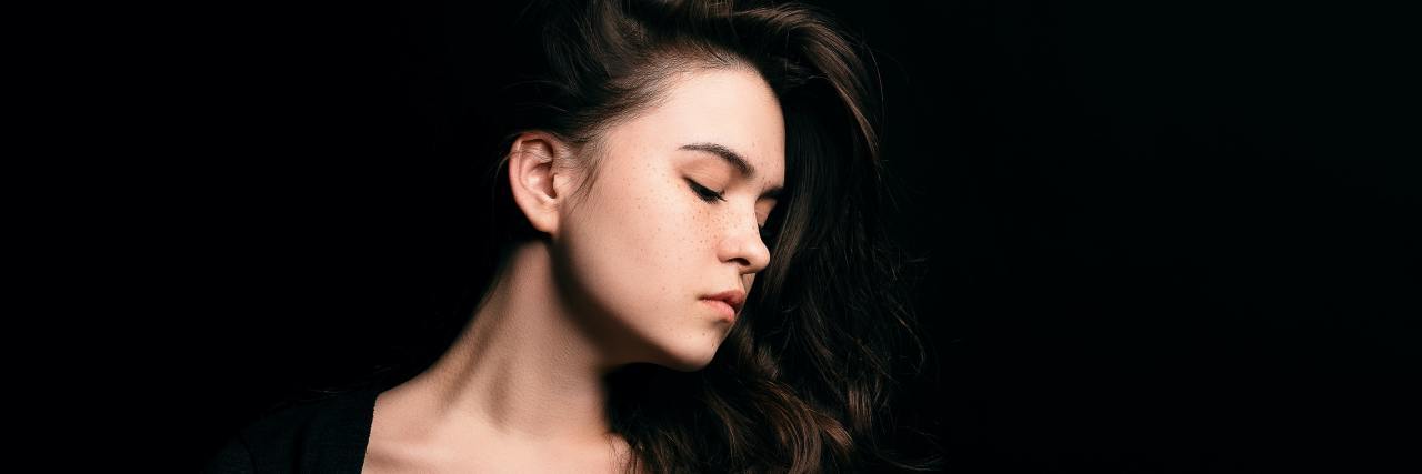 Let People Talk Openly About How They're Affected by COVID-19 Measures woman with her eyes closed and head turned, wearing a black shirt with a blackground