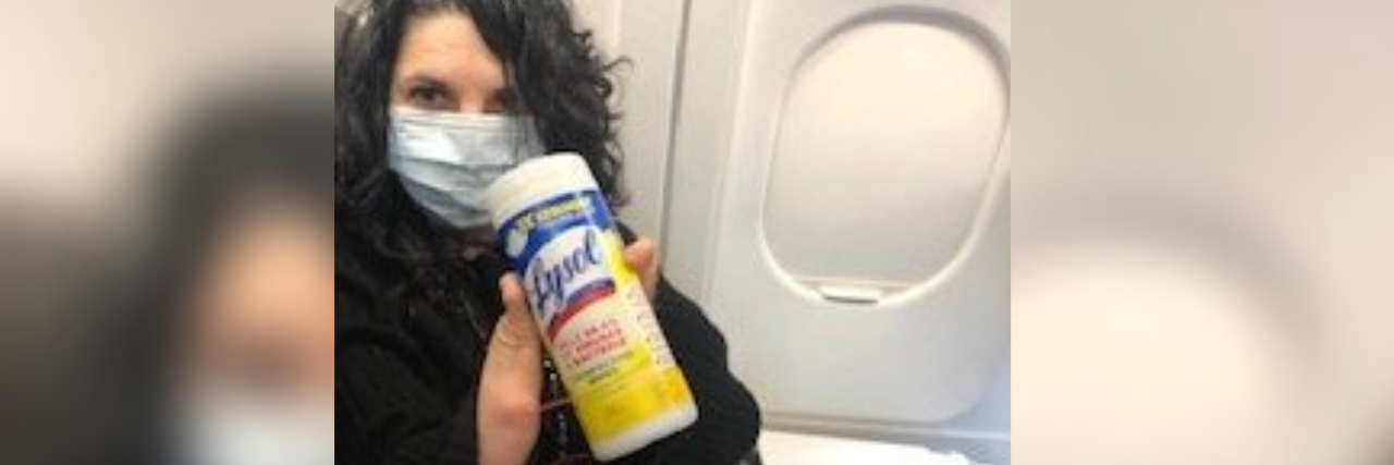 Rethinking the Handshake After the COVID-19 Pandemic Ends Meg on an airplane holding a container of Lysol wipes.