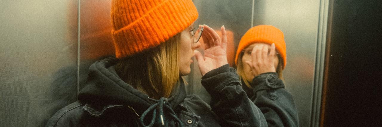 photo of woman looking into mirror in elevator and partially covering her face