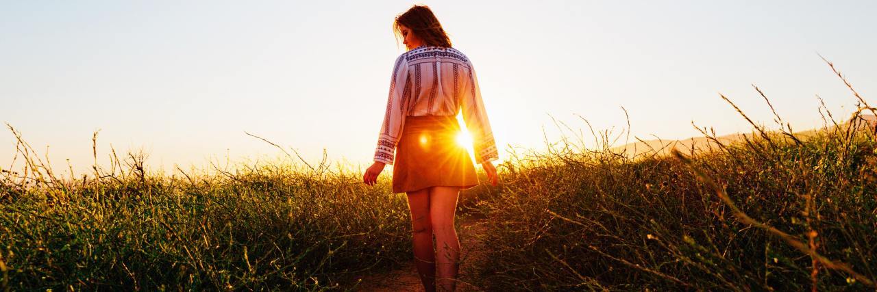 young woman walking in a field during sunset