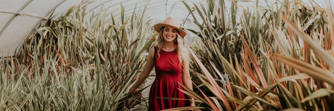 Taking My Life Back, Even in Self-Isolation With Mental Illness woman in a red dress with a sunhat on walking through a greenhouse smiling
