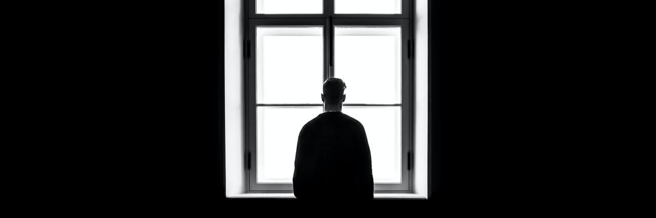 Discrimination in Social Work Against a Position in OCD Peer Support black and white photo of man in dark room silhouetted against window