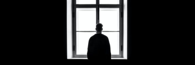 black and white photo of man in dark room silhouetted against window