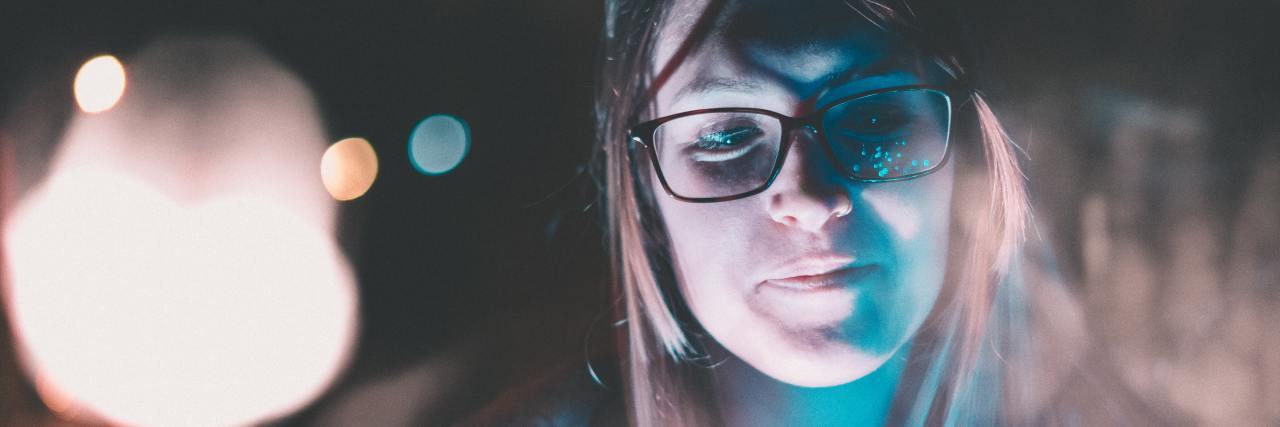 woman in glasses with a slight smile standing outside in the dark with lights around her