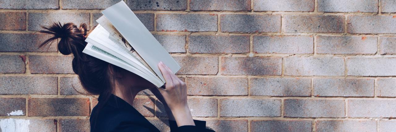 woman in a blazer standing in front of a brick wall with papers on her face