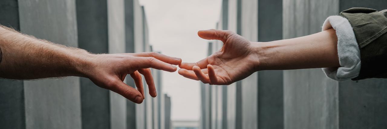 photo of two hands from unseen people reaching out to touch each other, with concrete pillars disappearing into distance at either side