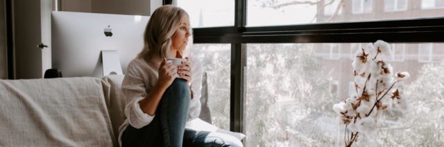 photo of woman sitting alone by window with a mug