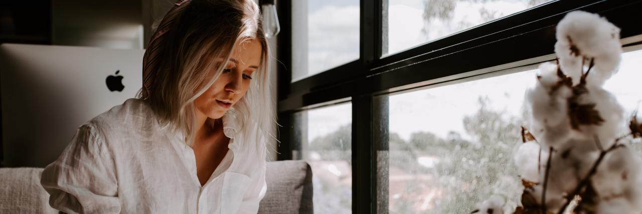 Don't Feel Guilty If You Find Being Productive Hard During COVID-19 woman sitting by a window writing in a journal