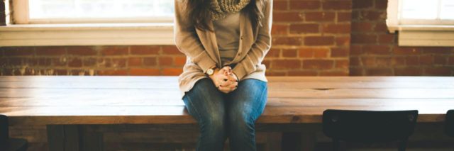 photo of woman in jeans sitting on wooden table with hands clasped on her lap
