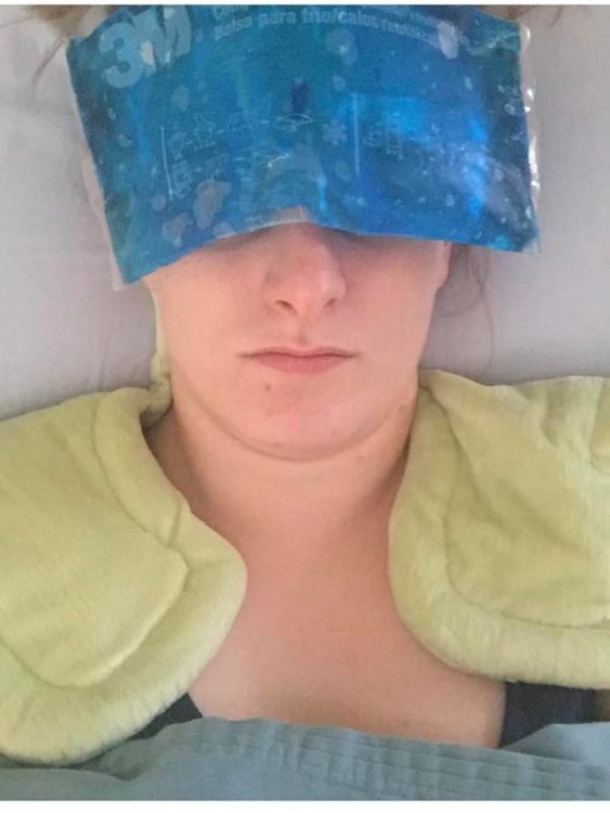 A woman lies down with heating pads on her shoulder and an ice pack covering her eyes