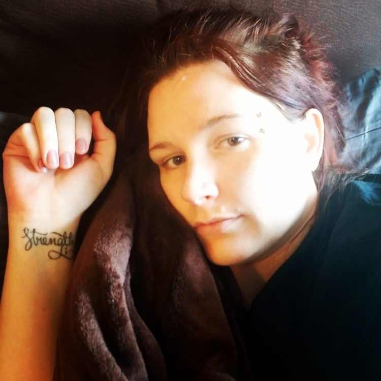 A woman with a tattoo with the word "strength" lies on a couch with a blanket