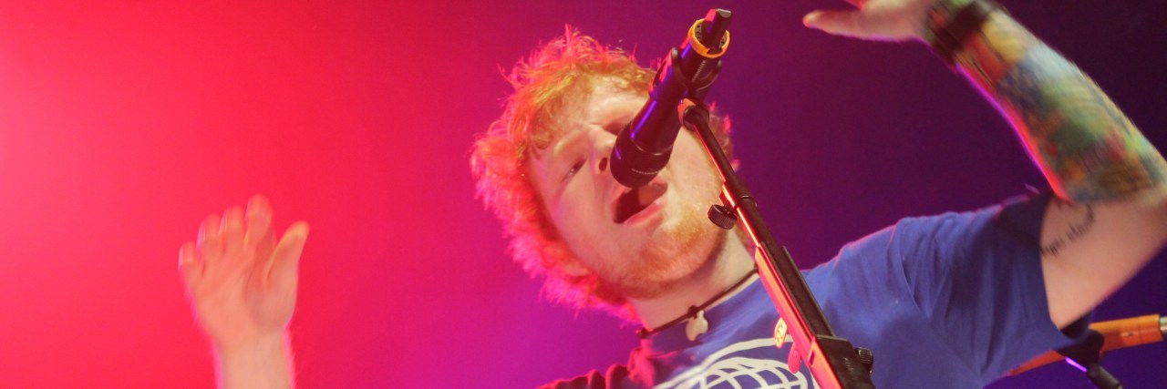 Ed Sheeran in a blue shirt sings onstage at a concert