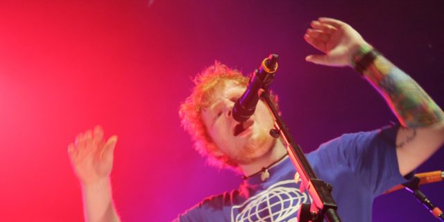 Ed Sheeran in a blue shirt sings onstage at a concert