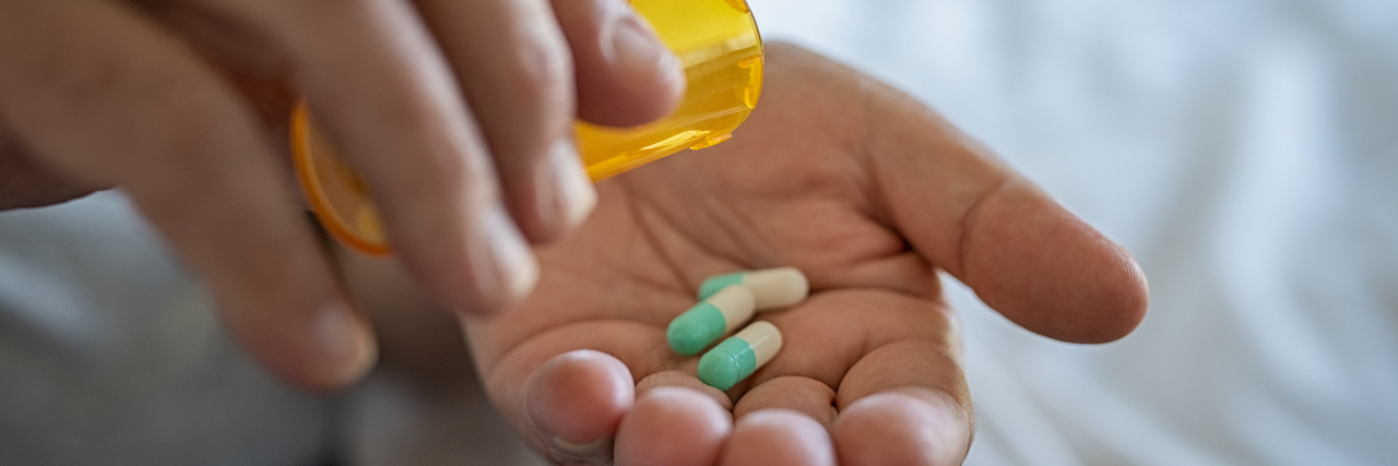 Do Antidepressants Cause Restless Leg Syndrome? Closeup of man hand pouring capsules from a pill bottle into hand.
