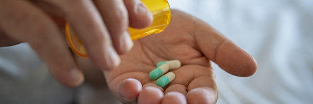 Closeup of man hand pouring capsules from a pill bottle into hand.