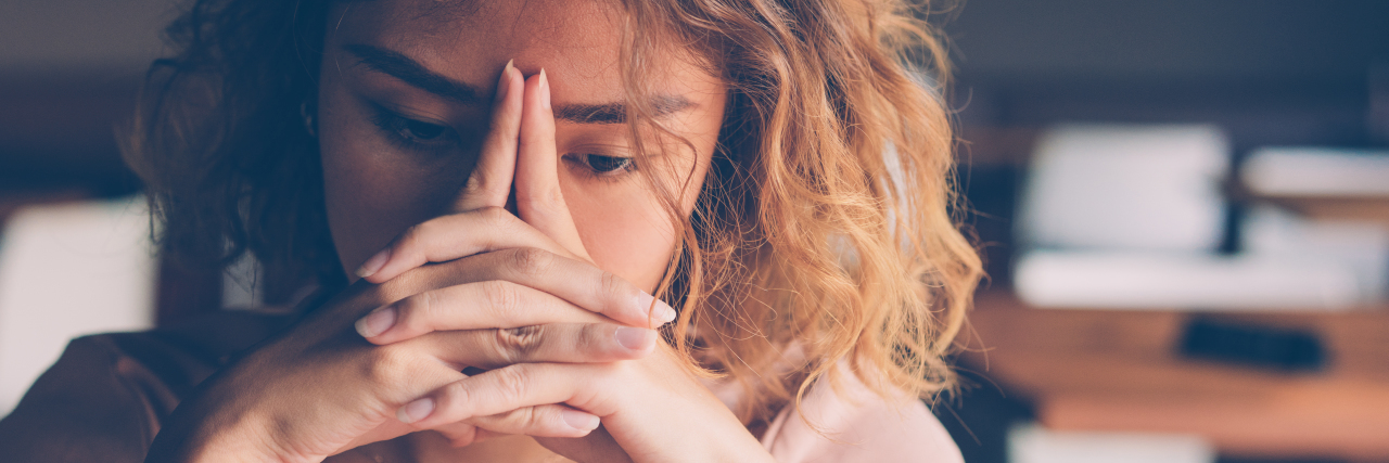 woman looking down, with her hands clasped against her face, feeling stressed