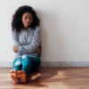 Portrait of black girl sitting on the floor of an empty room with her arms crossed and a forlorn expression on her face