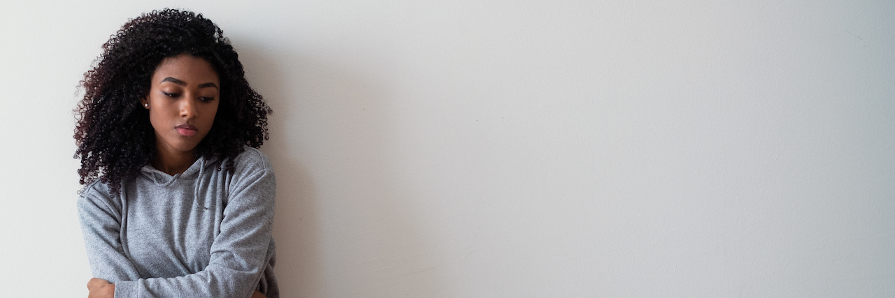 Excerpt From Jodi Aman's Book 'Anxiety . . . I’m So Done with You' Portrait of black girl sitting on the floor of an empty room with her arms crossed and a forlorn expression on her face