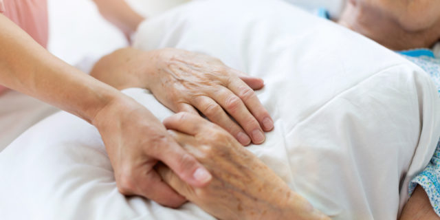 Daughter visiting her senior mother in hospital, holding hands
