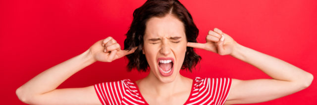 woman putting fingers into her ears, looking frustrated, wanting to scream