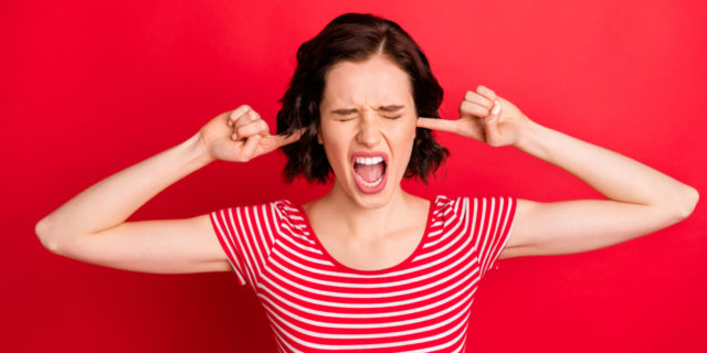 woman putting fingers into her ears, looking frustrated, wanting to scream