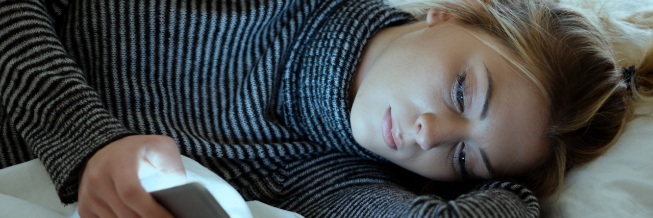 Sad woman using smartphone while lying in bed.