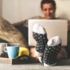Woman sitting on a couch in the living room with warm socks, coffee and laptop.
