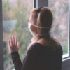 Woman wearing a mask looking out the window during the coronavirus pandemic.