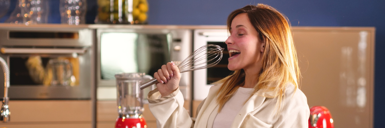 COVID-19 Shelter-in-Place Tips From a Person With Chronic Illness Woman in kitchen in pajamas singing.