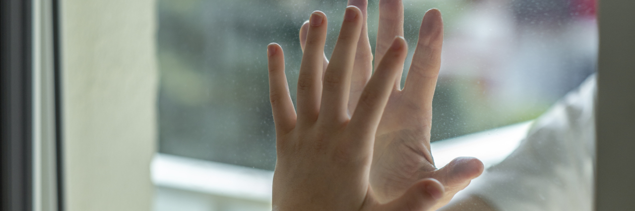Hands separated by a glass window for social distancing during the coronavirus lockdown.