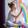 Sad little girl painting a rainbow on the window.