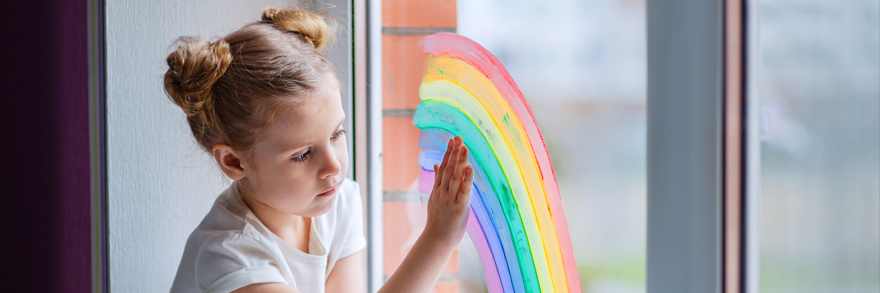 Sad little girl painting a rainbow on the window.