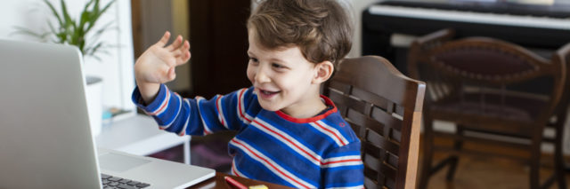 a young boy waving at a computer screen