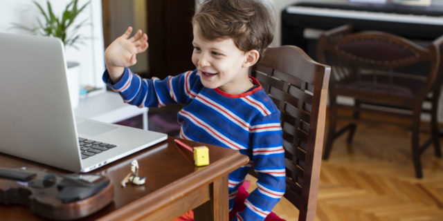 a young boy waving at a computer screen