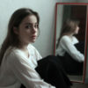 Portrait of young sad woman sitting near a mirror