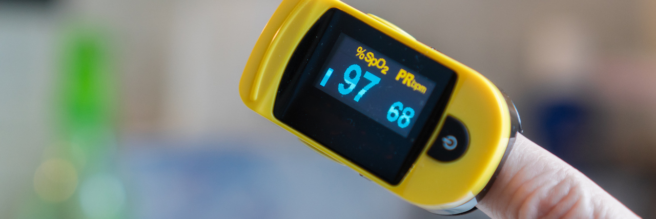 Close-up of hand with pulse oximeter attached to finger measuring blood oxygen and pulse rate