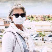 Senior woman wearing sunglasses and face mask outdoors.