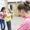 three girls are snickering at another little girl outside school