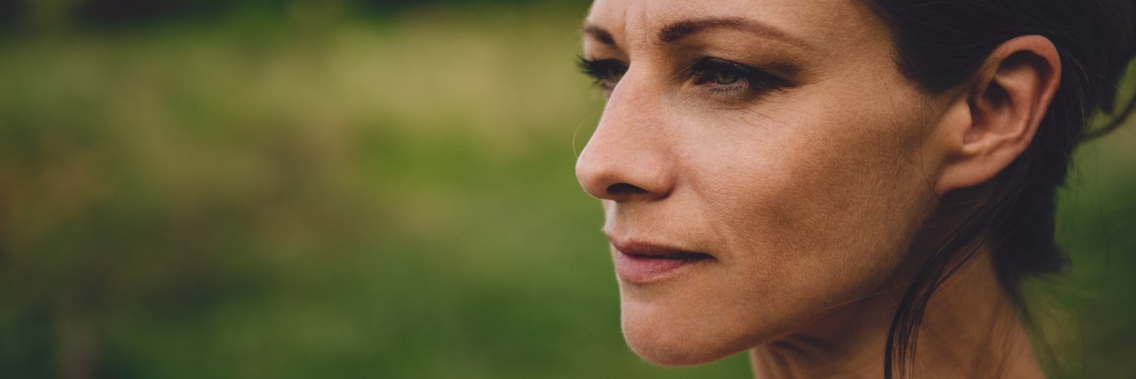 Why Sometimes Strangers, Not Friends, Support Your Mental Health Story Portrait of woman with brown hair and green eyes, standing outside and looking off in the distance