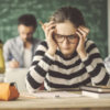 photo of student wearing glasses, resting head in her hands at desk