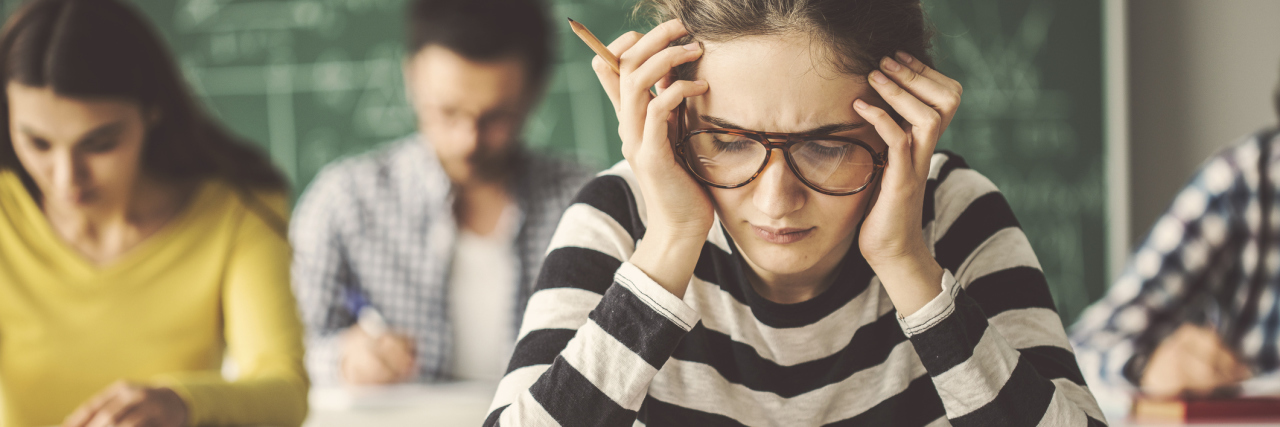 photo of student wearing glasses, resting head in her hands at desk