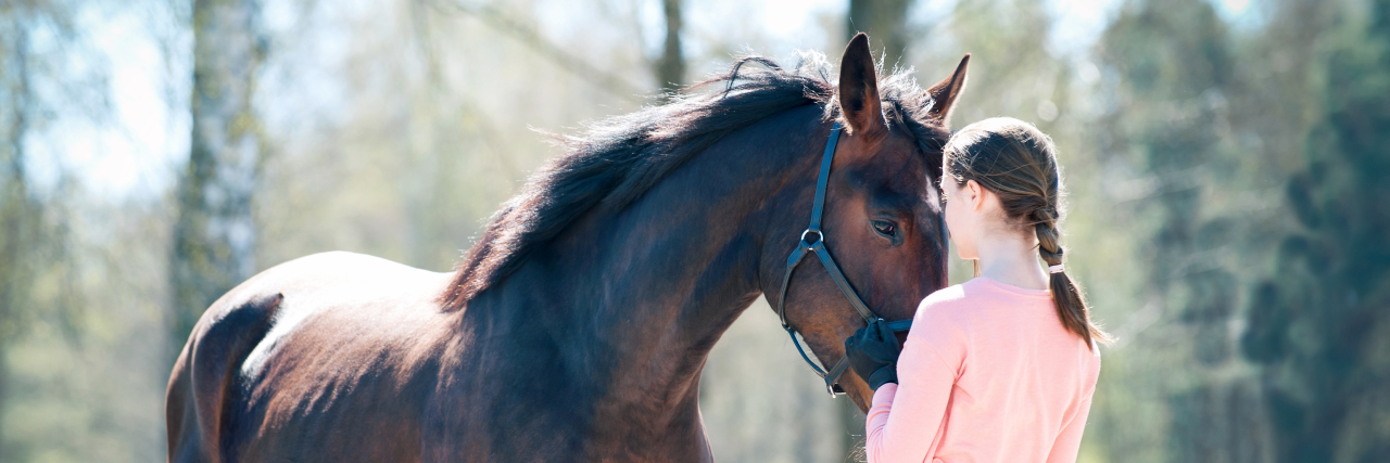 Young woman cuddling a dark brown horse.