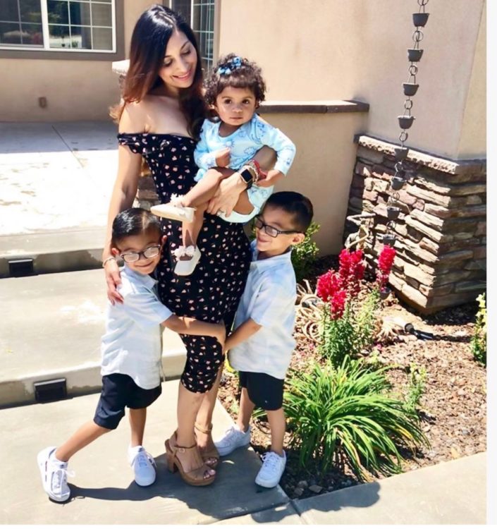 A mom is standing with her three little kids for a photo.