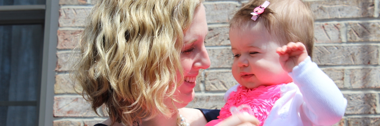 A mother is holding her infant daughter in her arms and smiling at her.