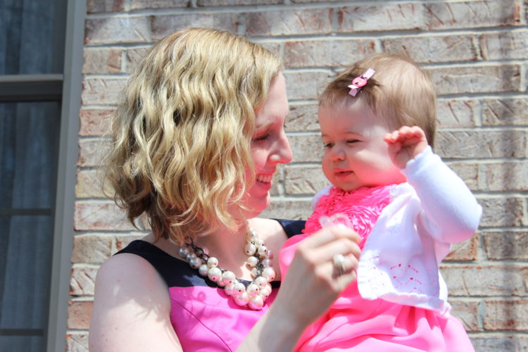 A mother is holding her infant daughter in her arms and smiling at her.