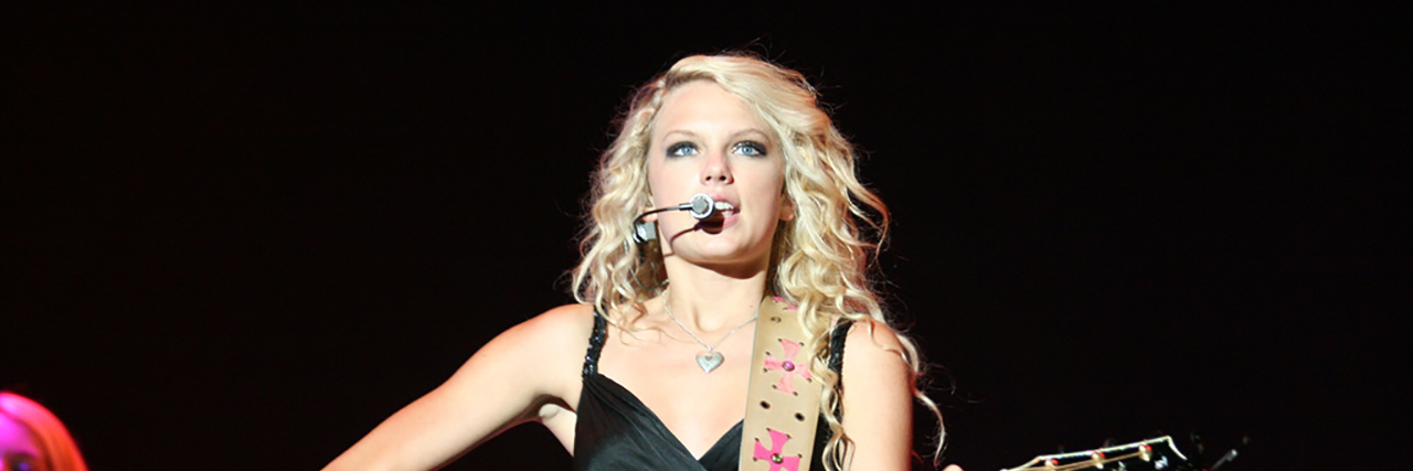 Taylor Swift: How Her Music Helps Me in My Life With Chronic Illness Taylor Swift sings onstage and plays the guitar in a black dress